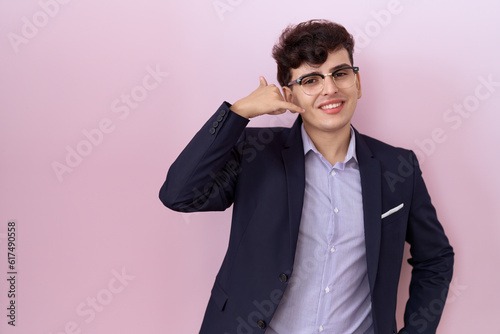 Young non binary man with beard wearing suit and tie smiling doing phone gesture with hand and fingers like talking on the telephone. communicating concepts.