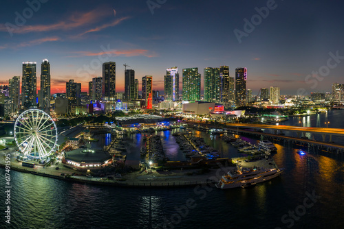 Aerial view of yachts in Miami marina at Bayside Marketplace with reflections in Biscayne Bay water and high illuminated skyscrapers of Brickell, city's financial center at night