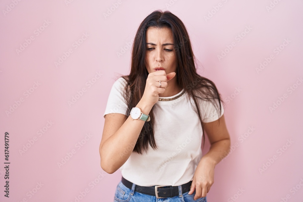 Young brunette woman standing over pink background feeling unwell and coughing as symptom for cold or bronchitis. health care concept. Young brunette woman standing over pink background feeling unwell and coughing as symptom for cold or bronchitis. health care concept.