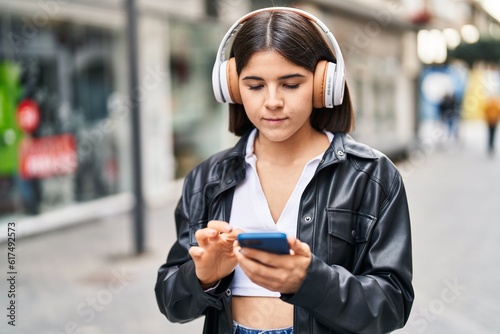 Young beautiful hispanic woman listening to music with serious expression at street