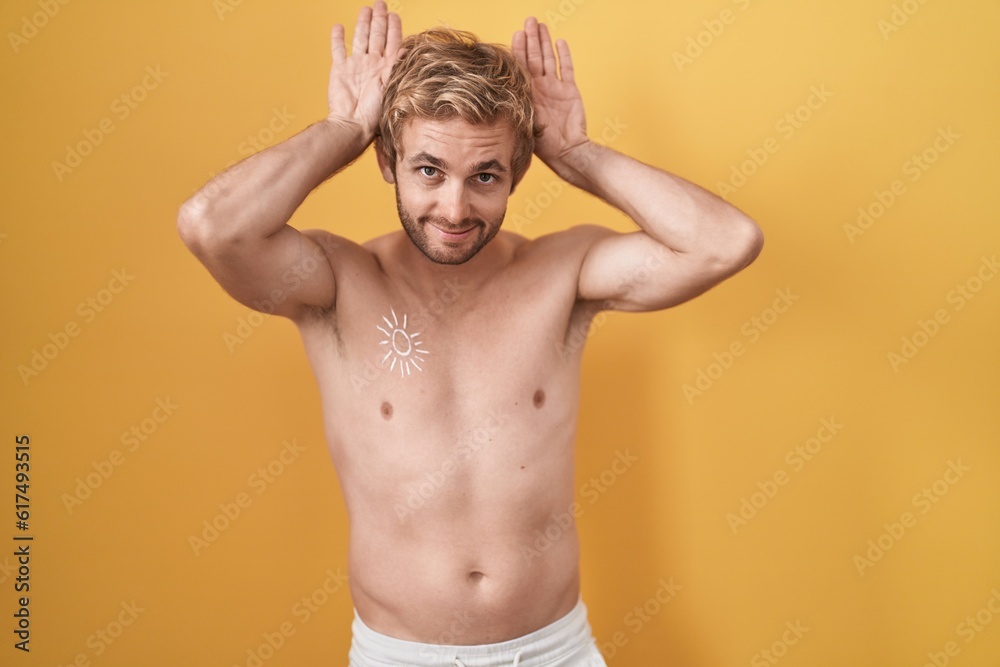 Fototapeta premium Caucasian man standing shirtless wearing sun screen doing bunny ears gesture with hands palms looking cynical and skeptical. easter rabbit concept.