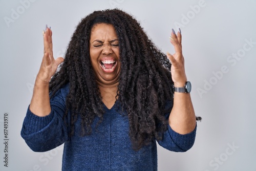 Plus size hispanic woman standing over white background celebrating mad and crazy for success with arms raised and closed eyes screaming excited. winner concept © Krakenimages.com