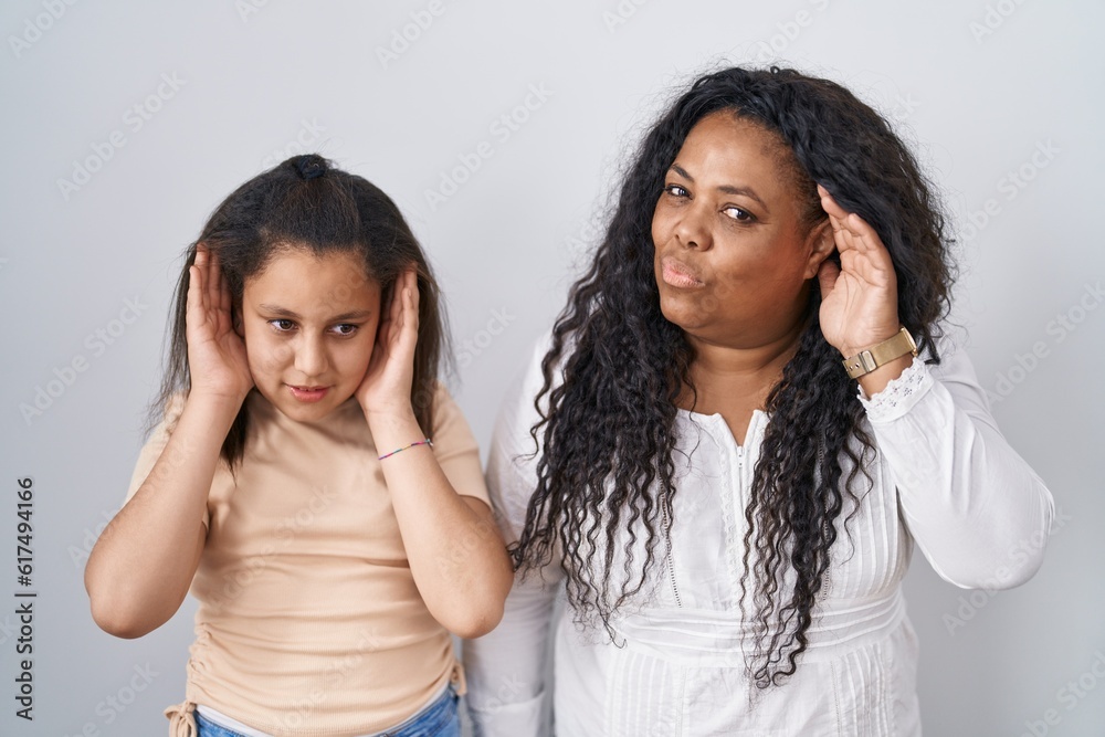 Mother and young daughter standing over white background trying to hear both hands on ear gesture, curious for gossip. hearing problem, deaf Mother and young daughter standing over white background trying to hear both hands on ear gesture, curious for gossip. hearing problem, deaf