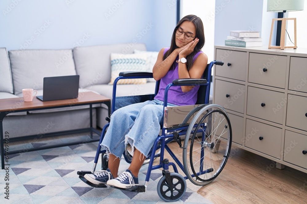 Φωτογραφία Young hispanic woman sitting on wheelchair at home sleeping tired dreaming and posing with hands together while smiling with closed eyes