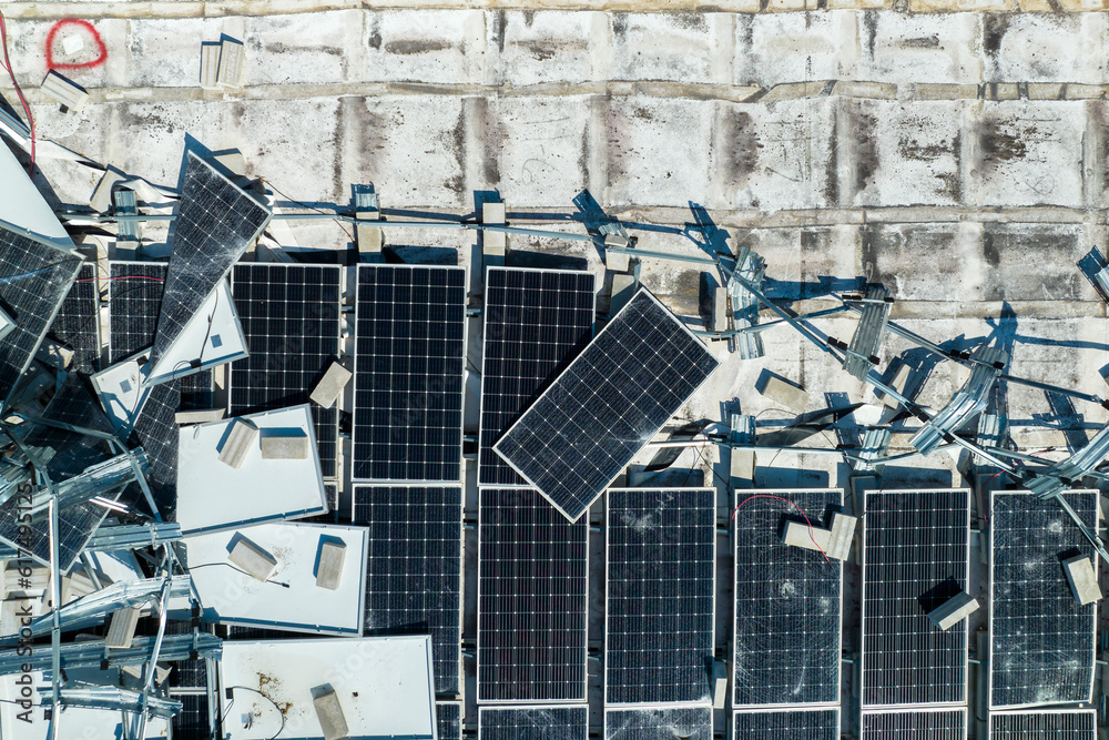 Obraz premium Top view of destroyed by hurricane Ian photovoltaic solar panels mounted on industrial building roof for producing green ecological electricity. Consequences of natural disaster in Florida