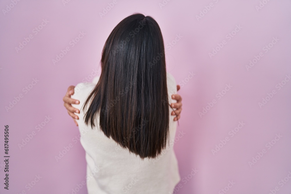 Young south asian woman standing over pink background hugging oneself happy and positive from backwards. self love and self care Young south asian woman standing over pink background hugging oneself happy and positive from backwards. self love and self care