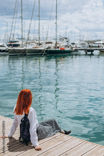 Carefree young tourist woman sitting on the seaside and enjoying bay view at the shore. Summer vacation abroad. Happiness, chilling concept.  Travelling. popular Spanish resort near Mediterranean sea