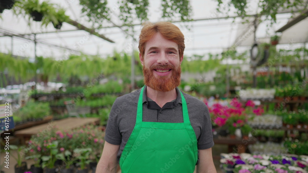 Portrait of a happy redhead male worker wearing Green apron standing inside flower shop. Local business concept of man employee Portrait of a happy redhead male worker wearing Green apron standing inside flower shop. Local business concept of man employee