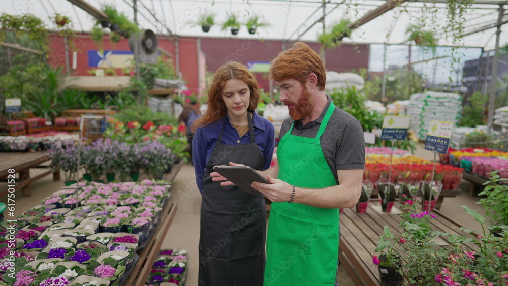 Male Staff Sharing Inventory Data on Tablet with Female Colleague in Flower Shop. Two Employees Engaging in Retail Tech Interaction. Local Business Concept Male Staff Sharing Inventory Data on Tablet with Female Colleague in Flower Shop. Two Employees Engaging in Retail Tech Interaction. Local Business Concept