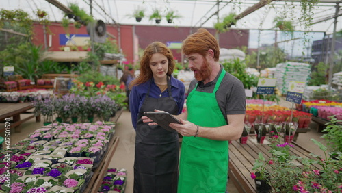 Male Staff Sharing Inventory Data on Tablet with Female Colleague in Flower Shop. Two Employees Engaging in Retail Tech Interaction. Local Business Concept