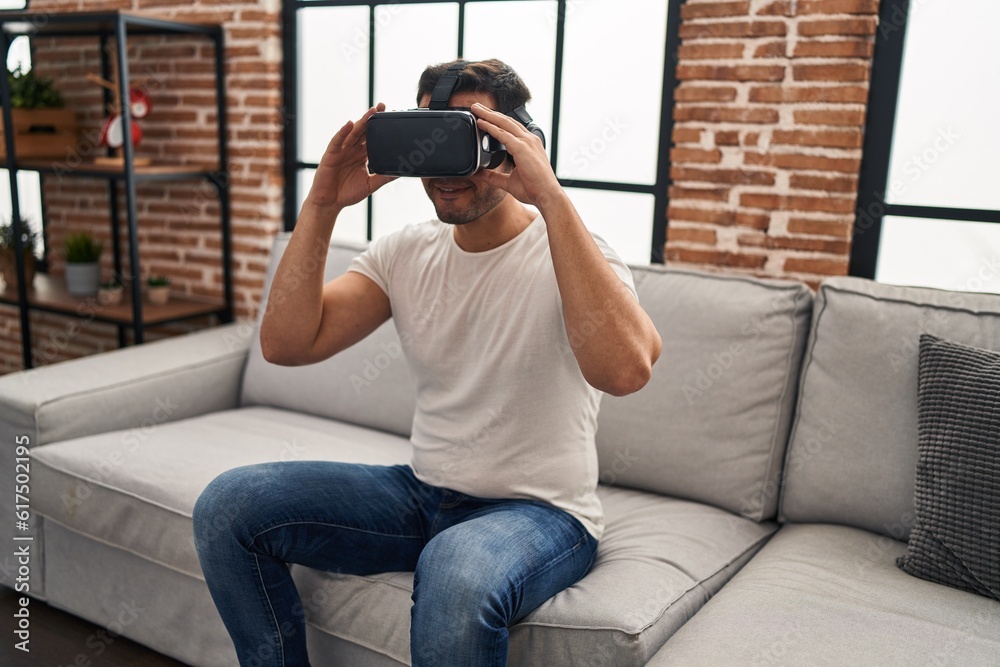 Fototapeta premium Young hispanic man playing video game using virtual reality glasses at home