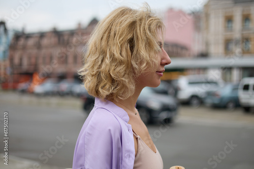 Portrait of a beautiful white woman walking down the street in the city center. Attractive young adult female with curly blonde hair on a walk