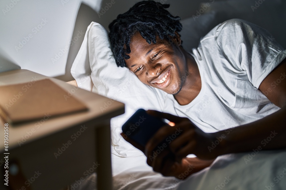 Fototapeta premium African american man using smartphone lying on bed at bedroom