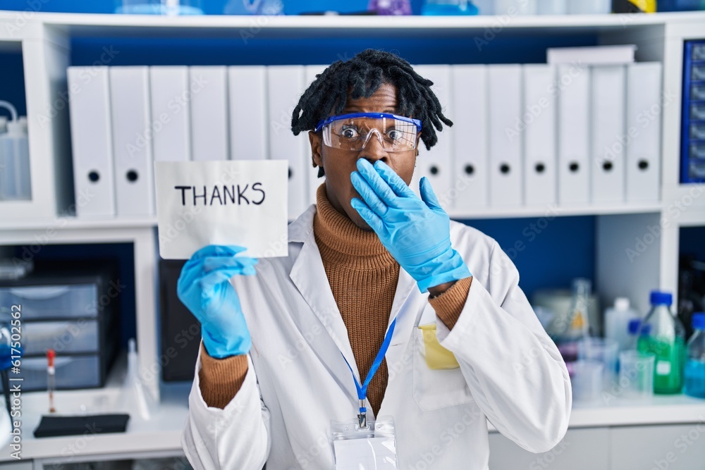 Young african man with dreadlocks working at scientist laboratory covering mouth with hand, shocked and afraid for mistake. surprised expression Young african man with dreadlocks working at scientist laboratory covering mouth with hand, shocked and afraid for mistake. surprised expression