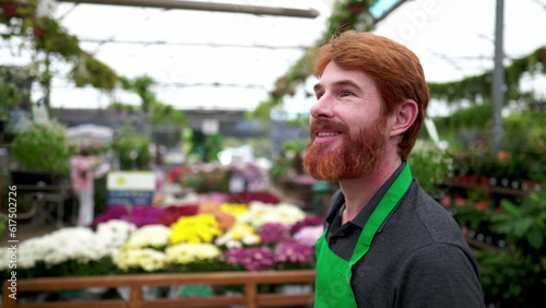 One Happy young man employee walking through plant store wearing green apron. A caucasian male staff face close-up walks through flower shop isle
