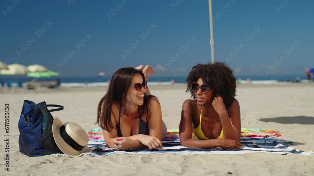 Two female friends chatting while laying down at beach
