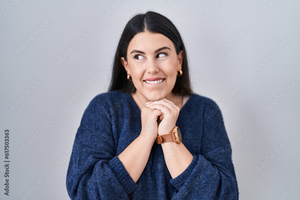 Young brunette woman standing over isolated background laughing nervous and excited with hands on chin looking to the side Young brunette woman standing over isolated background laughing nervous and excited with hands on chin looking to the side