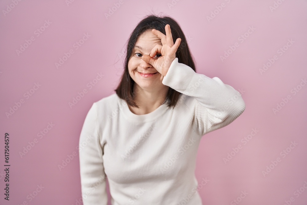 Woman with down syndrome standing over pink background doing ok gesture with hand smiling, eye looking through fingers with happy face. Woman with down syndrome standing over pink background doing ok gesture with hand smiling, eye looking through fingers with happy face.