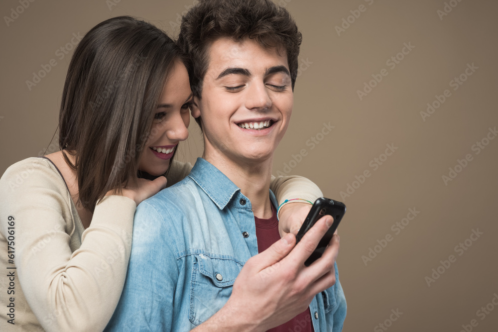 Fototapeta premium Cheerful young teen smiling couple with mobile phone enjoying together