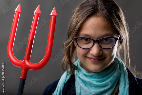 portrait of a little rascal girl with a red pitchfork meaning she is a little devil ready to make some pranks and jokes to have some fun