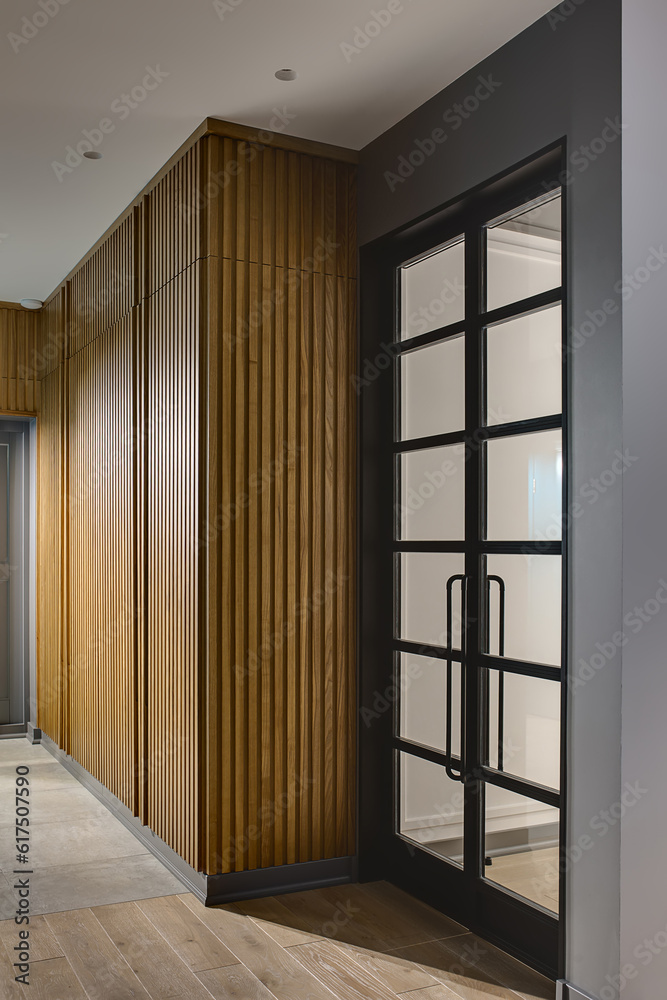 Glowing hall in a modern style with gray walls and tiles with a parquet on the floor. There is a large wooden wardrobe, gray door and glass black door. Vertical.