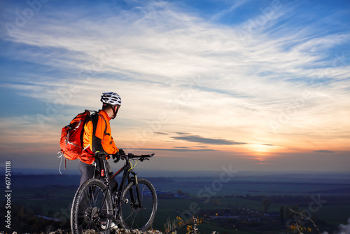 cyclist on mountain-bike at sunset, cyclist on the background of beautiful sunset. cyclist with white helmet and red backpack. beautiful landscape. back view.