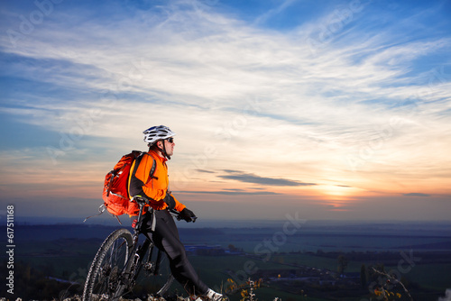 Cyclist on the top of a hill looking at sunrise. Traveler on bike with red backpack riding in mountains. Freedom concept.