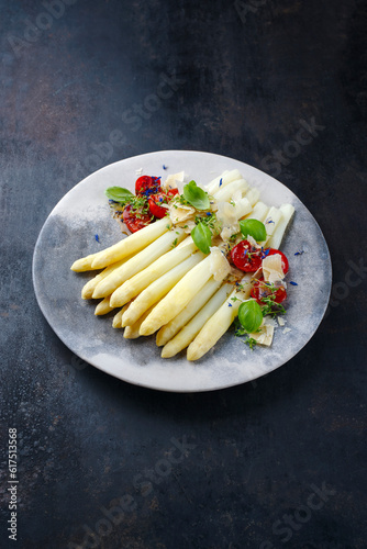 White asparagus glazed with cherry tomatoes and parmesan cheese served as close-up on a design plate with text space