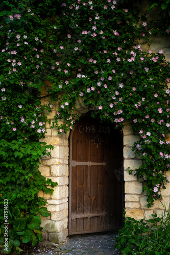 Zabytkowe mury i wejście do klasztoru przez drewniane zdobione drzwi. Kolorowe kwiaty na zabytkowym murze.  © smoku7979