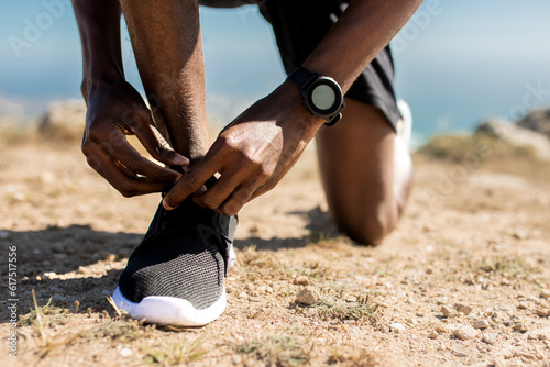 Training, healthy lifestyle concept. Closeup view of unrecognizable black man tying his shoelaces before jogging outdoors