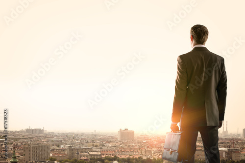 Businessman standing with back against morning city, panoramic view