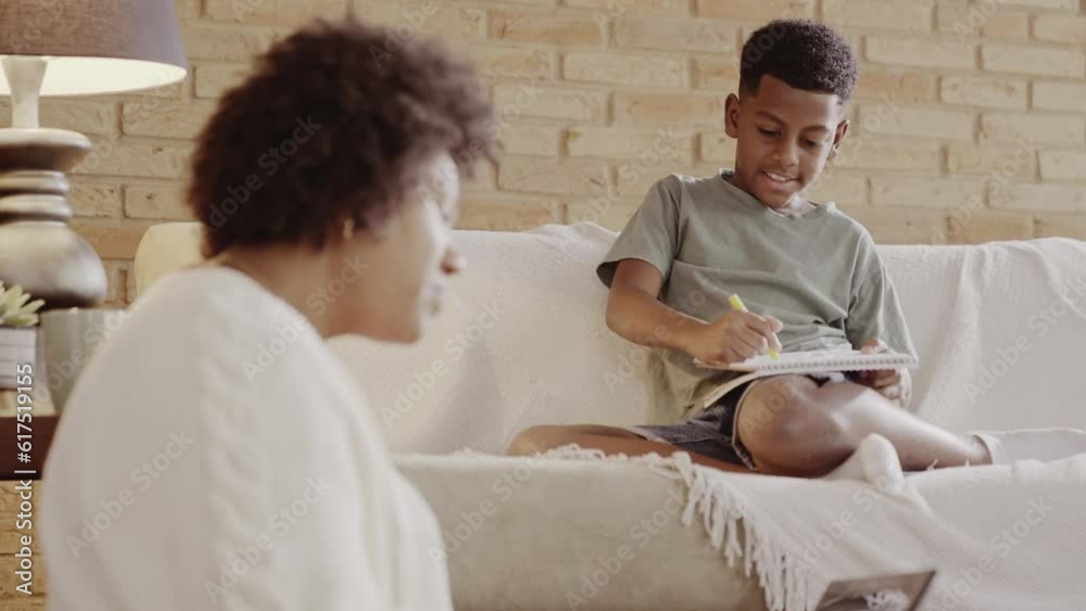mae Brasileira ajudando seu filho com a licao de casa enquanto trabalha usando o computador sentada no chao da sala de sua casa no Brasil