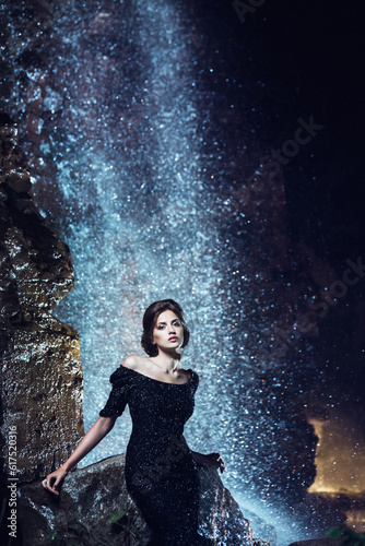 Beautiful woman in black dress posing near waterfall