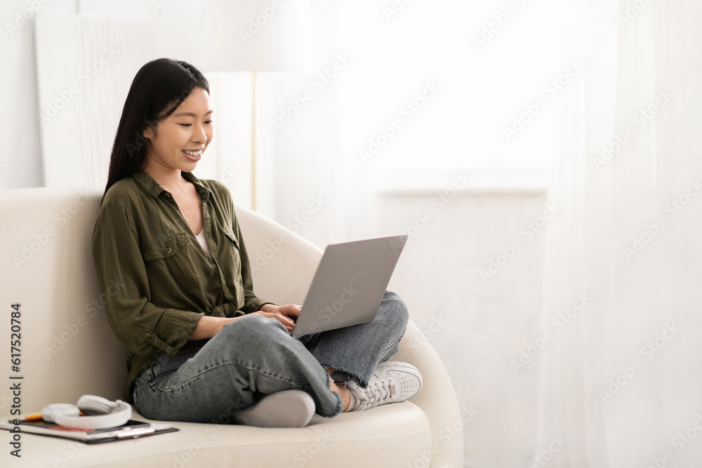 Smiling chinese woman sitting on couch with computer Smiling chinese woman sitting on couch with computer