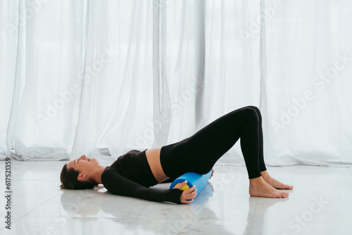 Pilates and massage. Woman with foam roller on floor for body tension and support during yoga class in gym.