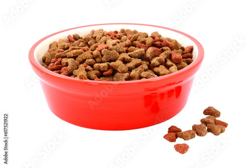 Dry cat food in a red bowl, some biscuits spilled beside, isolated on a white background