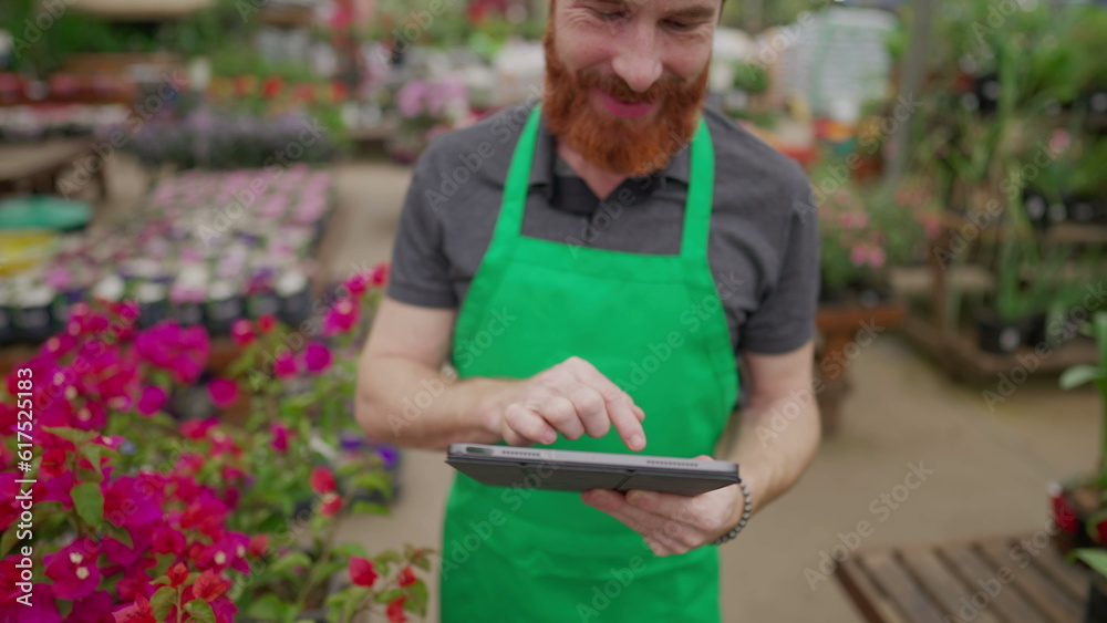 Fototapeta premium Close-up of staff_s hand holding tablet browsing inventory inside local business. Young man wearing green apron using modern technology at Flower Shop