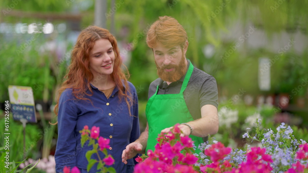 A male employee helping customer to pick flower inside Plant Store. A caucasian florist staff standing next to woman wearing Green apron
