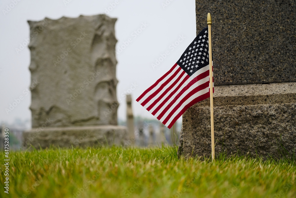 Closeup on American flag places my cemetery gravestone on grey cloudy day with selective focus