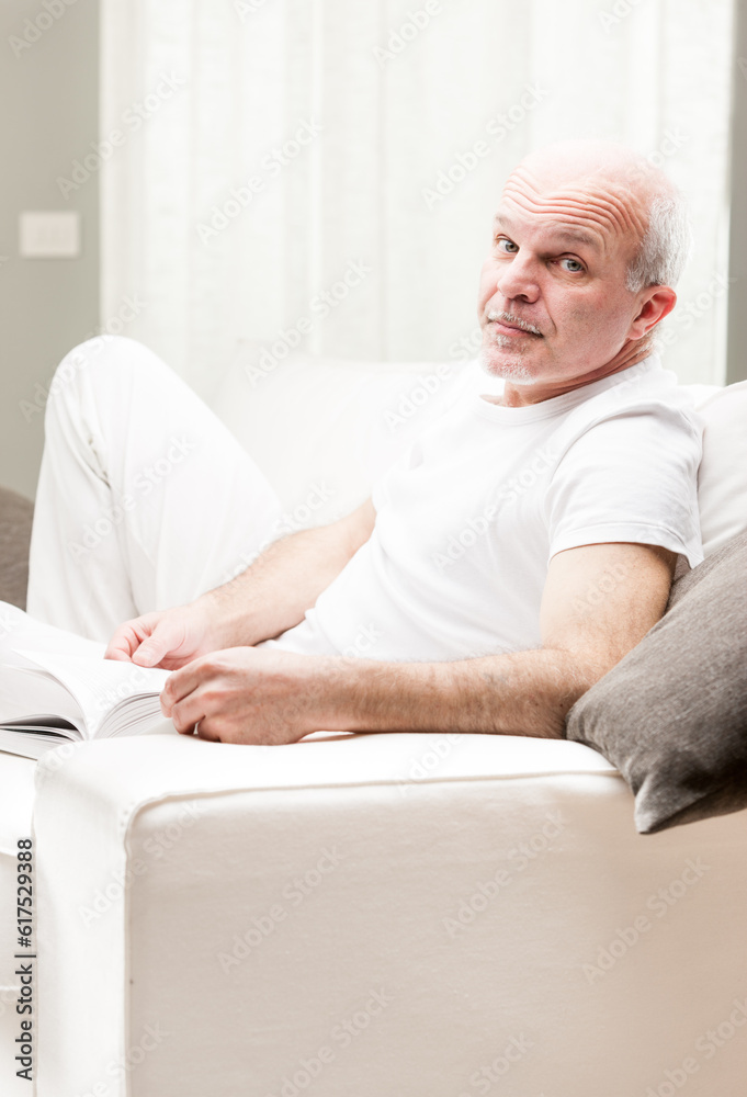 senior man gets himself educated and has fun reading a book, relaxed on his couch in his living room senior man gets himself educated and has fun reading a book, relaxed on his couch in his living room