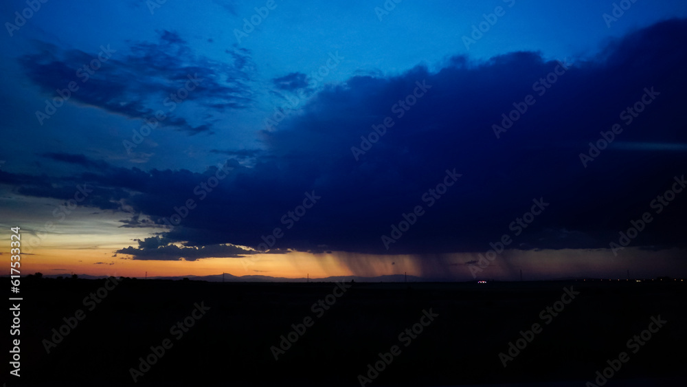 storm clouds at sunset with bursts of rain in the distance on the horizon and a line of reddish sky