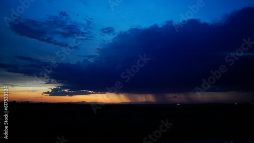 storm clouds at sunset with bursts of rain in the distance on the horizon and a line of reddish sky © cribea