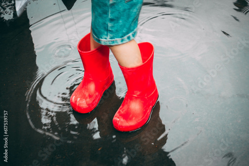 child in red rubber boots holds paper ships in his hands