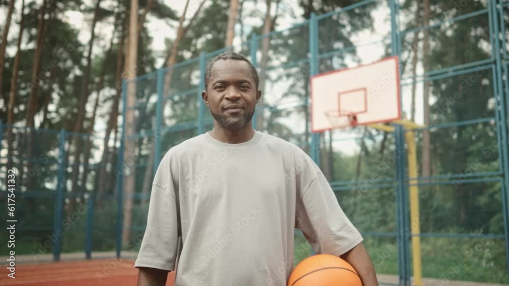 Camera moving to joyful mature man standing on outdoor basketball court