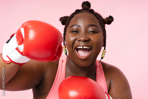 Closeup body positive African woman wearing red boxing gloves isolated on pink background © Maria Vitkovska