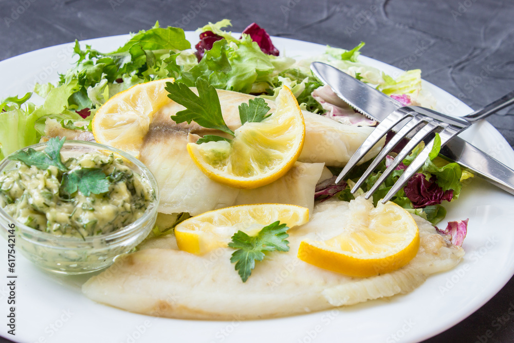 steamed tilapia fish with salad and tartar sauce with appliances on dark background