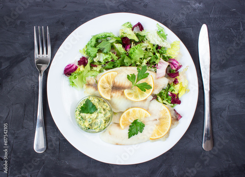steamed tilapia fish with salad and tartar sauce with appliances on dark background. vertical