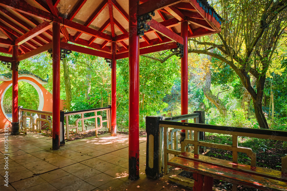 Red Chinese style pavilion in lush greenery of asian part of tropical botanical garden in Lisbon, Portugal