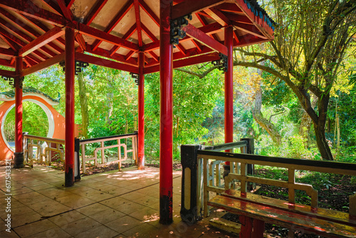 Red Chinese style pavilion in lush greenery of asian part of tropical botanical garden in Lisbon, Portugal