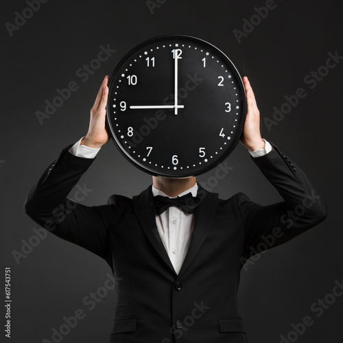 Handsome young man wearing a tuxedo and holding a clock